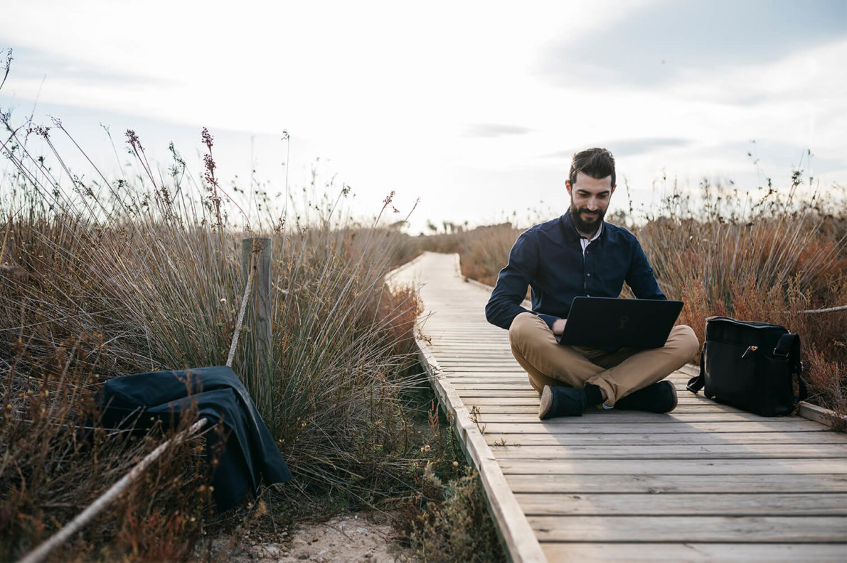 Man seated with laptop on boardwalk